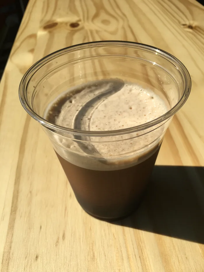 A cup of creamy nitro cold brew on a sunlit wooden table